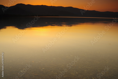 夕暮れの湖。湖面に映る黄昏の空と山並みのシルエットから成る静寂の印象。