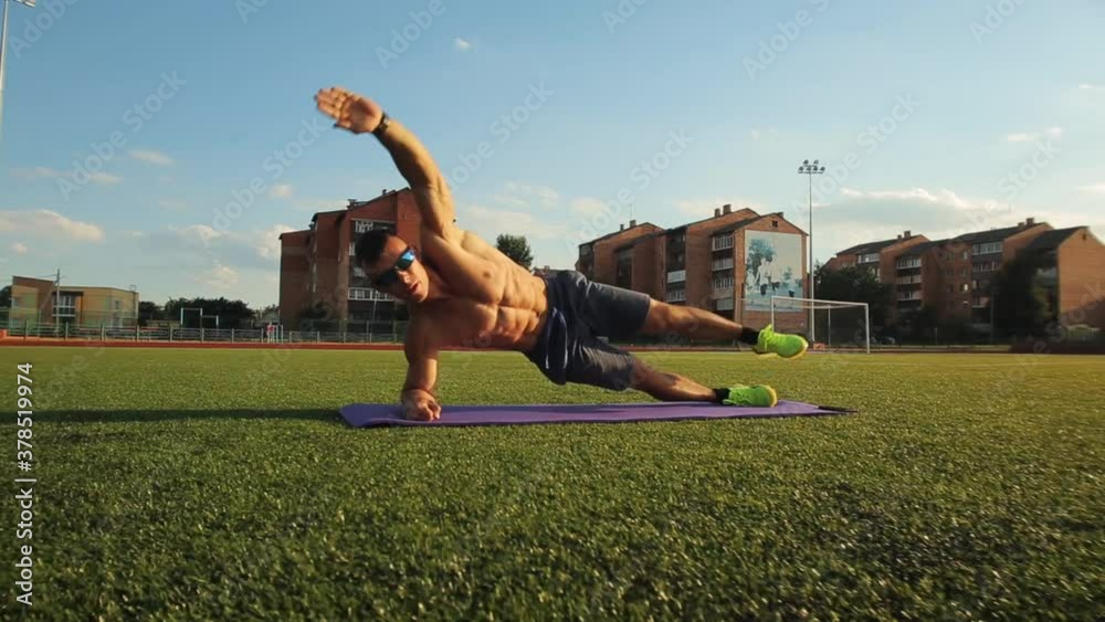 A muscular man with a naked torso trainIng in a city stadium and does swing legs while standing in a side plank. Close-up. Camera moves forward backward A muscular man with a naked torso trainIng in a city stadium and does swing legs while standing in a side plank. Close-up. Camera moves forward backward