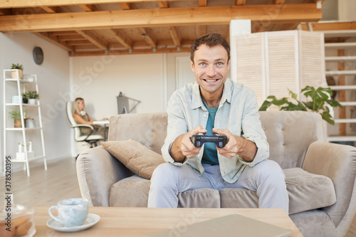 Excited happy man sitting on sofa with joystick and playing in computer games in the living room