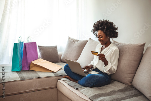 Shot of a cheerful young woman doing online shopping while seating  on a couch at home during the day. Cropped shot of a young woman using a credit card to make an online payment at home