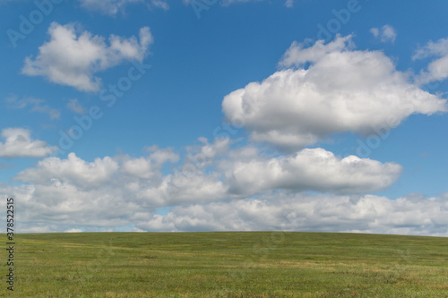 white bright fluffy light clouds in blue sky with green grass field, open space