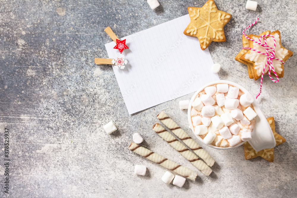 Christmas background. White list and cup of hot cocoa with marshmallows and Christmas baking on a stone countertop. Top view flat lay background. Copy space. Christmas background. White list and cup of hot cocoa with marshmallows and Christmas baking on a stone countertop. Top view flat lay background. Copy space.