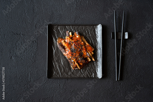 Eggplant slices in a spicy red sauce decorated black sesame seeds on dark concrete background. Top view. Asian food