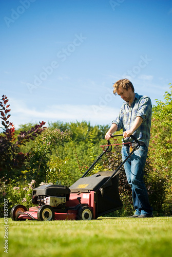 Young man mowing the lawn on a sunny spring day