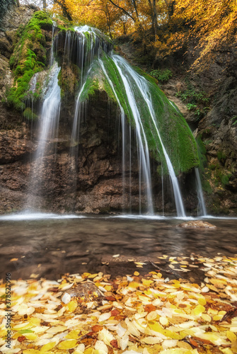 Multi-stream waterfall with green moss in the autumn forest with yellow leaves