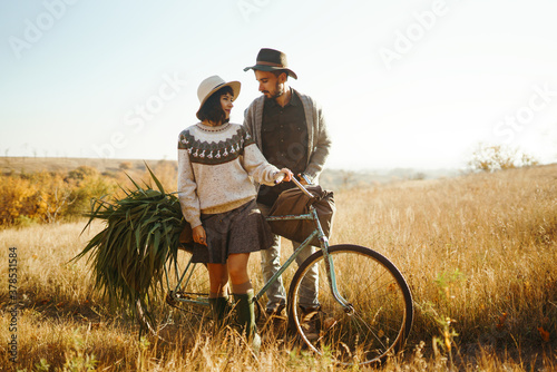 Lovely hipster couple with bike. Stylish and loving couple wearing hats and sweaters enjoying each other in the park.The concept of youth, love, autumn and lifestyle.