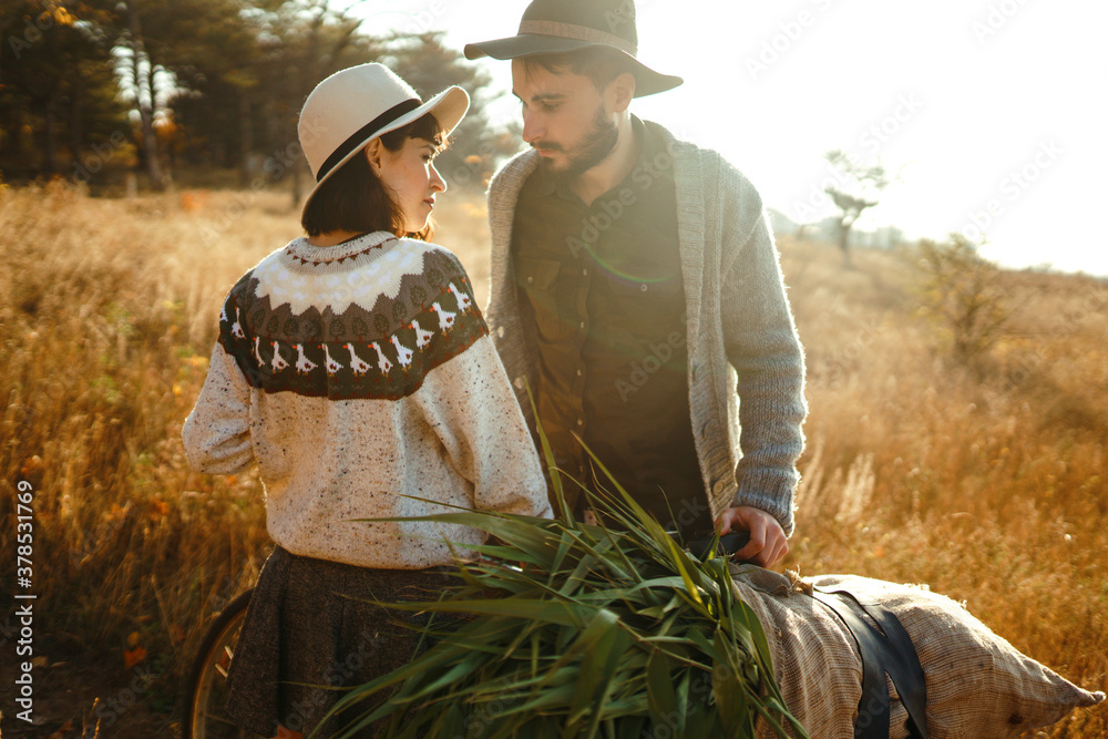 Lovely hipster couple with bike. Stylish and loving couple wearing hats and sweaters enjoying each other in the park.The concept of youth, love, autumn and lifestyle. Lovely hipster couple with bike. Stylish and loving couple wearing hats and sweaters enjoying each other in the park.The concept of youth, love, autumn and lifestyle.