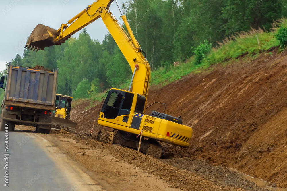 Road widening works (highway construction). Crawler excavator digs the ground with a bucket. Road widening works (highway construction). Crawler excavator digs the ground with a bucket.