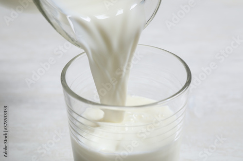 Pouring milk into glass on white table, closeup