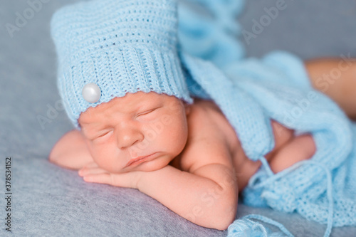 Adorable newborn baby wrapped in a beautiful fabric, woolen scarf and with a small hat on his head © Valeriya