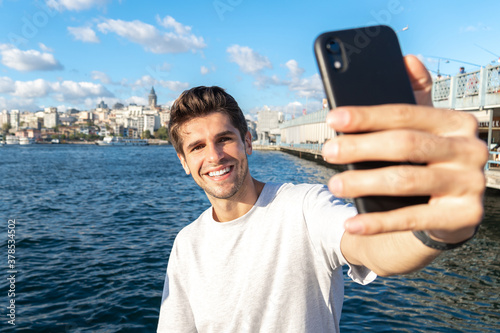 Young handsome man is taking a selfie with his phone near Galata bridge tourist spot 