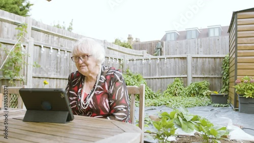 Elderly Woman talking elatedly on Skype on a tablet device in the garden day photo