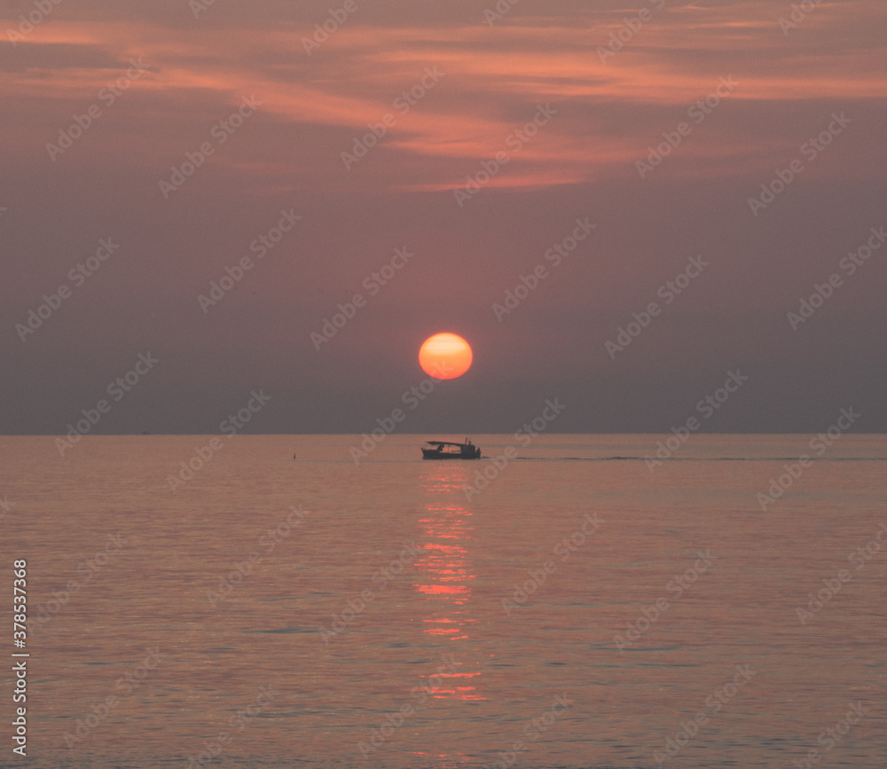 Barca en el mar debajo del sol en el amanecer