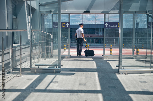 Male pilot with travel suitcase standing outside airport terminal