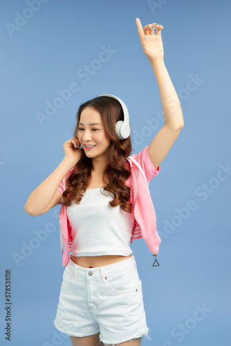 Pretty cool girl having fun and listens to music in the headphones  dancing over blue background.