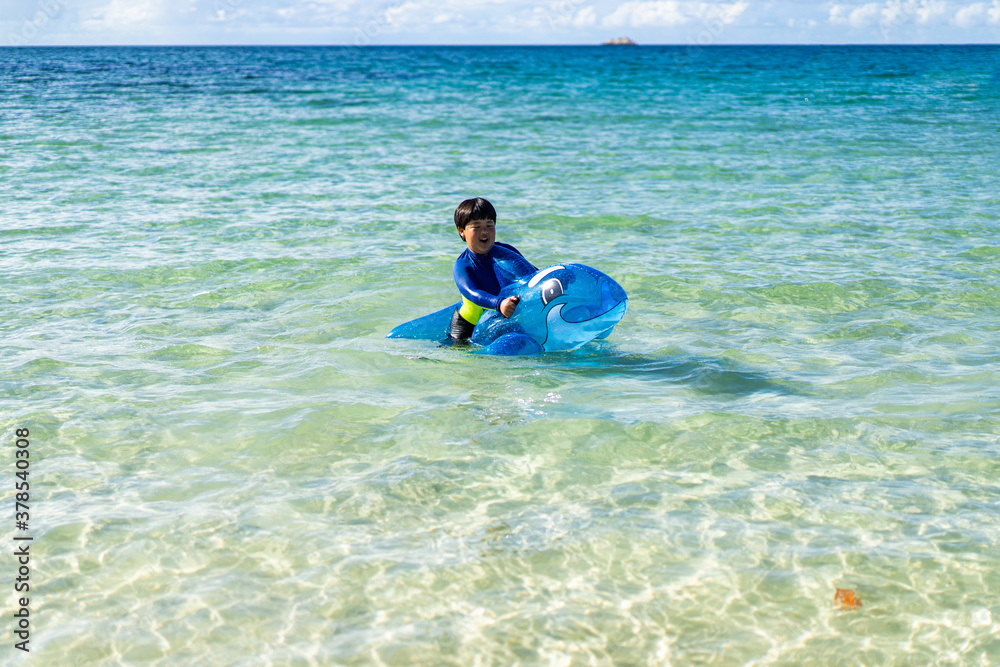 A Little baby boy with inflatable toy float playing in the water on summer vacation in a tropical resort. Kid with toy shark on a beach holiday.