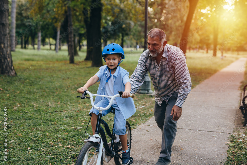 Obraz premium little boy teaching to drive a bike with his grandfather in the park