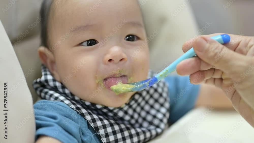 Asian 8 months baby boy eating blend food on a high chair, Mother feeds a Little Baby with a Spoonful of food. Asian 8 months baby boy eating blend food on a high chair, Mother feeds a Little Baby with a Spoonful of food.