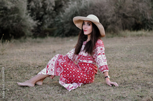 Beautiful girl with Oriental appearance in a red long sundress, hat in the Park