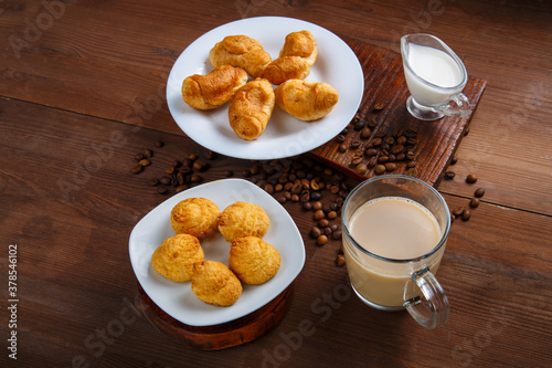 A mug with coffee and a jug of cream and croissants and cookies on the table among the scattered coffee beans.