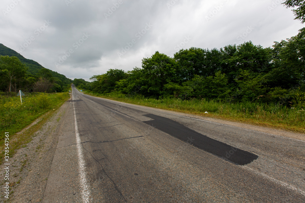 Fototapeta premium Very bad road in Russia. The asphalt road is all in holes in the middle of the forest.