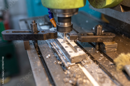 Execution of the work process on an industrial milling machine. The metal part is clamped in the collet. The cutter makes a longitudinal groove. Coolant is supplied. Metal shavings fly to the sides.