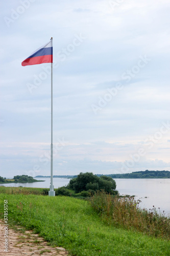 view with flag of russian federation on high flagpole on the green shore of volhov river