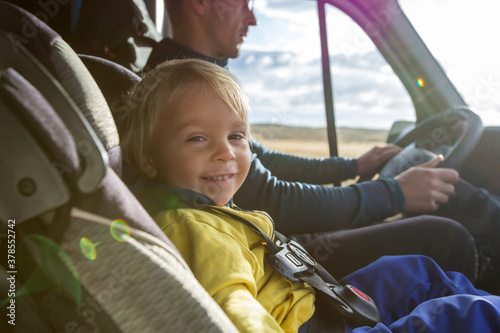 Cute toddler boy, kid sitting on the front seat in child seat on big camper van, smiling