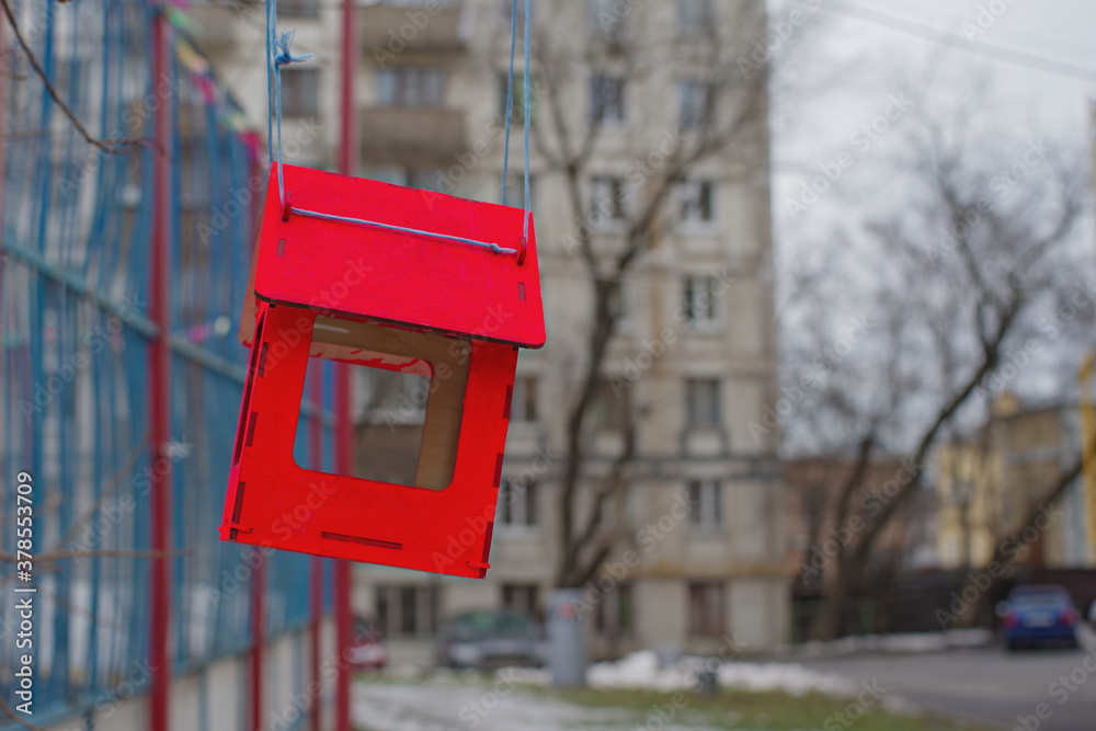 Bright red bird feeder hanging on a tree branch in a city courtyard. Children's сare for birds in difficult winter times. Bright red bird feeder hanging on a tree branch in a city courtyard. Children's сare for birds in difficult winter times.