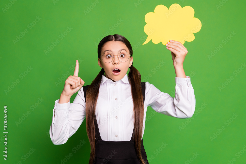 Photo portrait of surprised excited shocked girl holding yellow thought bubble card pointing finger up isolated on vivid green colored background