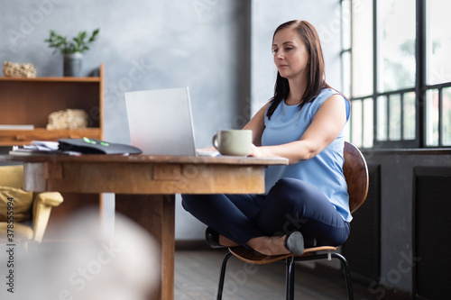 Beautiful relaxing businesswoman sitting near table in lotus pose working on laptop
