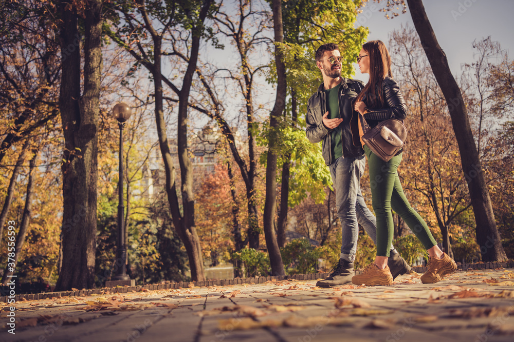 Obraz premium Full body profile side photo of positive couple go in autumn september town center park path speak wear jacket rucksack