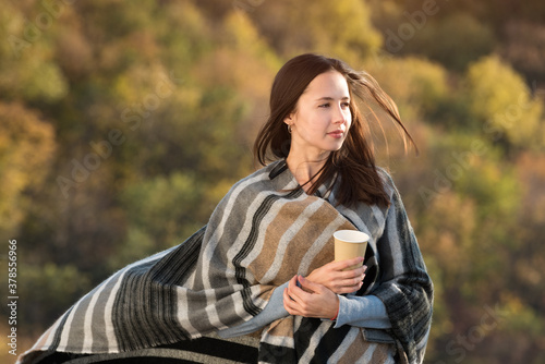 Pretty young woman wrapped in a blanket and looks into the distance. Autumn weather.