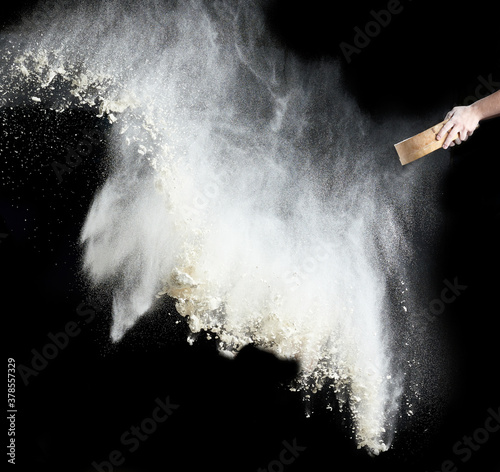 female hand sifts white wheat flour through a round wooden sieve on a black background