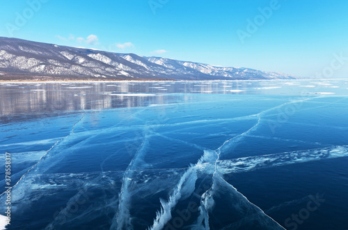 Landscape typical of winter Baikal Lake with beautiful blue smooth ice and snow-capped coastal mountains in February. Natural background. Winter ice travel on the lake  focus on ice 