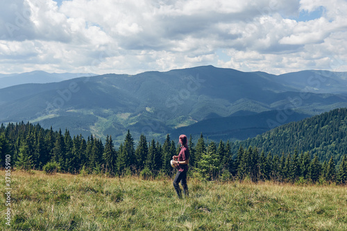 Girl with pink hair climbs uphill mountain. Hiking through forest in summer. Standing on the clearing and looks at the mountains. Dark autumn forest. Local Travel
