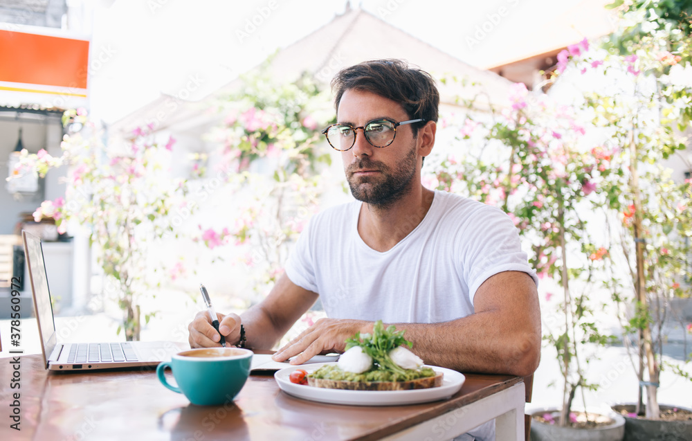 Thoughtful man writing thoughts in notebook during lunchtime