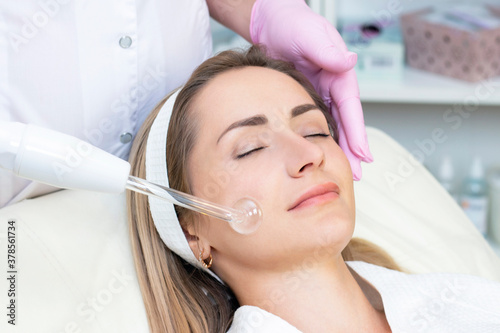 Cosmetologist performs a pulse current procedure for the face of a young woman. close