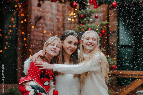 Three pretty teen girls in winter sweaters posing at back yard under the snow. photo