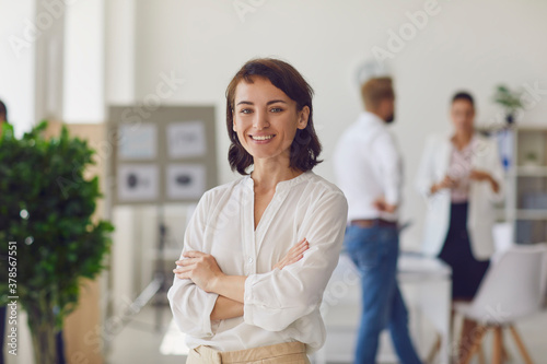Happy successful business lady or company employee standing in office looking at camera and smiling photo