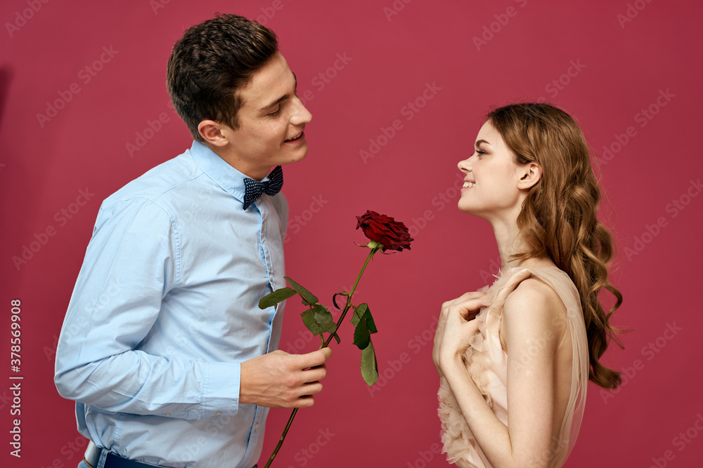 enamored man and woman with a red flower on a pink background hug each other Copy Space
