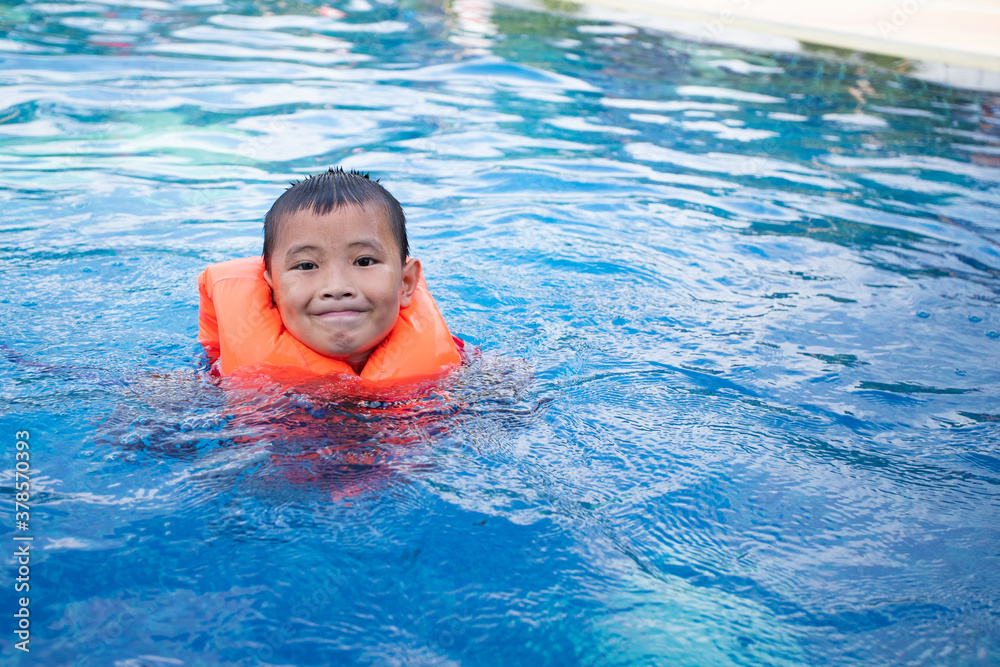 Asian boy in swimsuit and life jacket swimming in the pool