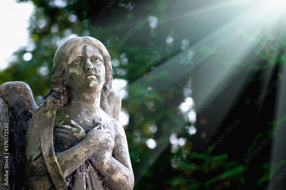 Obraz premium Fragment of ancient stone statue of guardian angel in rays of light