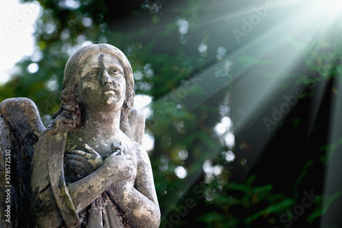 Fragment of ancient stone statue of guardian angel in rays of light