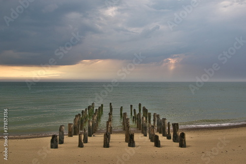 Abandoned and collapsed wooden pier on the sandy Baltic sea shore. Stormy clouds over the sea