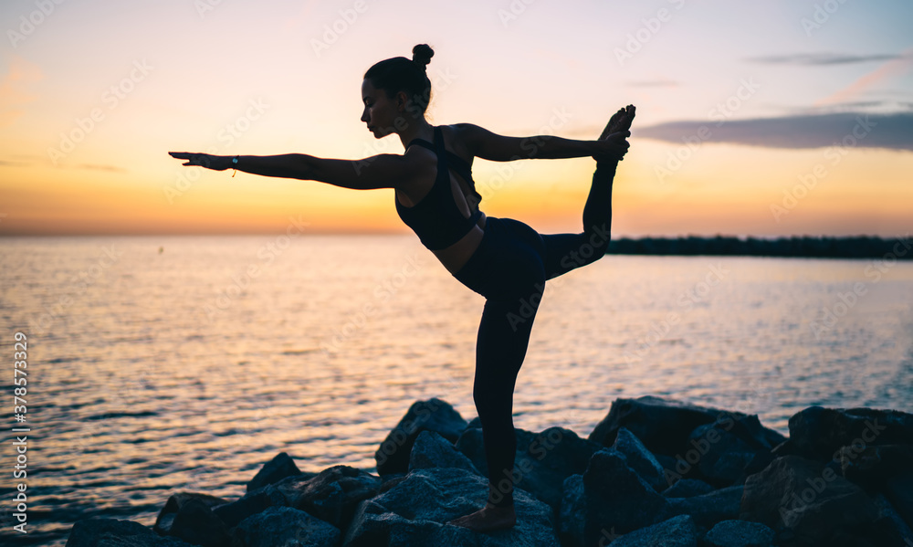 Slim woman doing yoga on coast at sunset