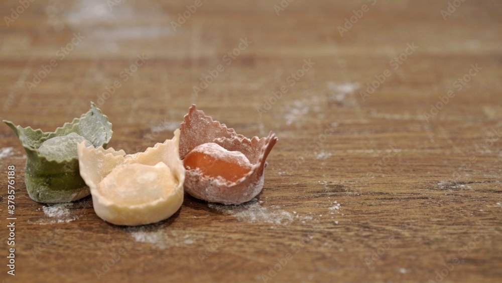 Fototapeta premium Three raw uncooked italian green, white and red ravioli on wooden table, italian flag colour. Close up of raw italian tortellini in flour on restaurant kitchen table