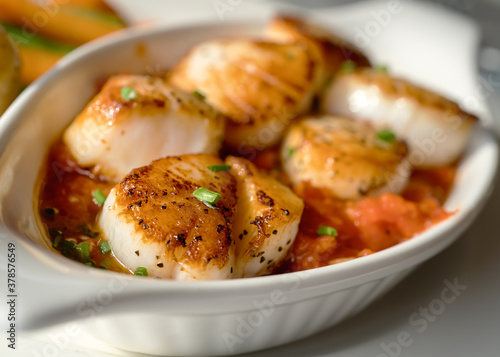 Freshly prepared sauteed scallops in a dish with tomato sauce and chives and a side of vegetables.