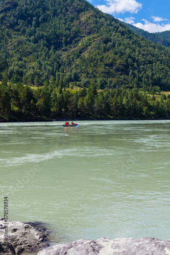 Colorful landscape of the river with a raft boat on the background of mountains covered with green forest and blue sky on a summer sunny day.