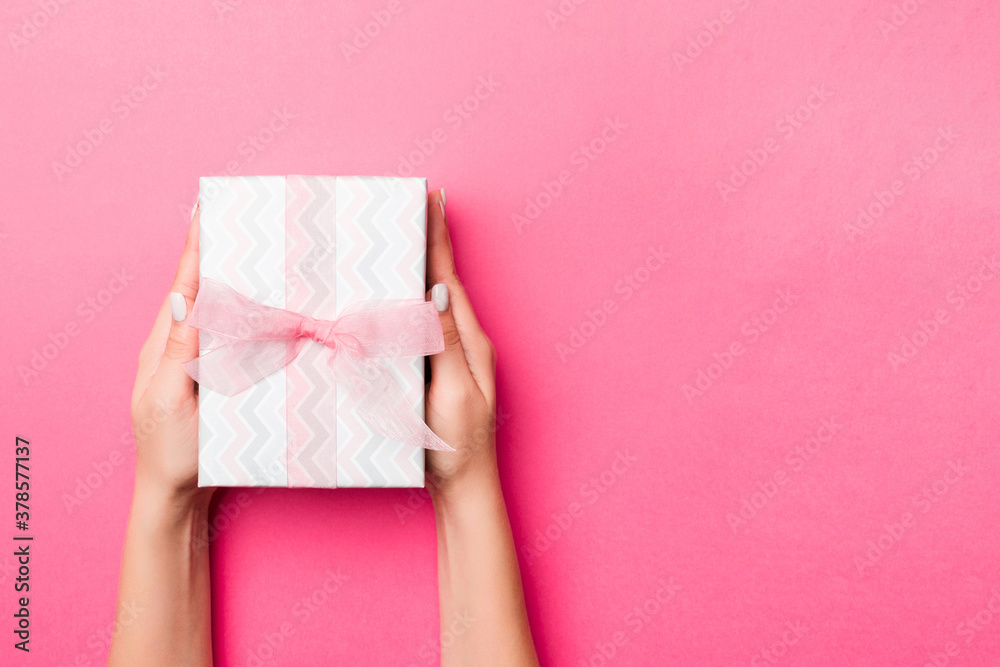 Girl Hands holding craft paper gift box with as a present for Christmas or other holiday on pink background, top view with copy sppace